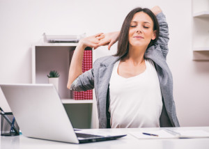 Young businesswoman is relaxing in her office. She is stretching her body.